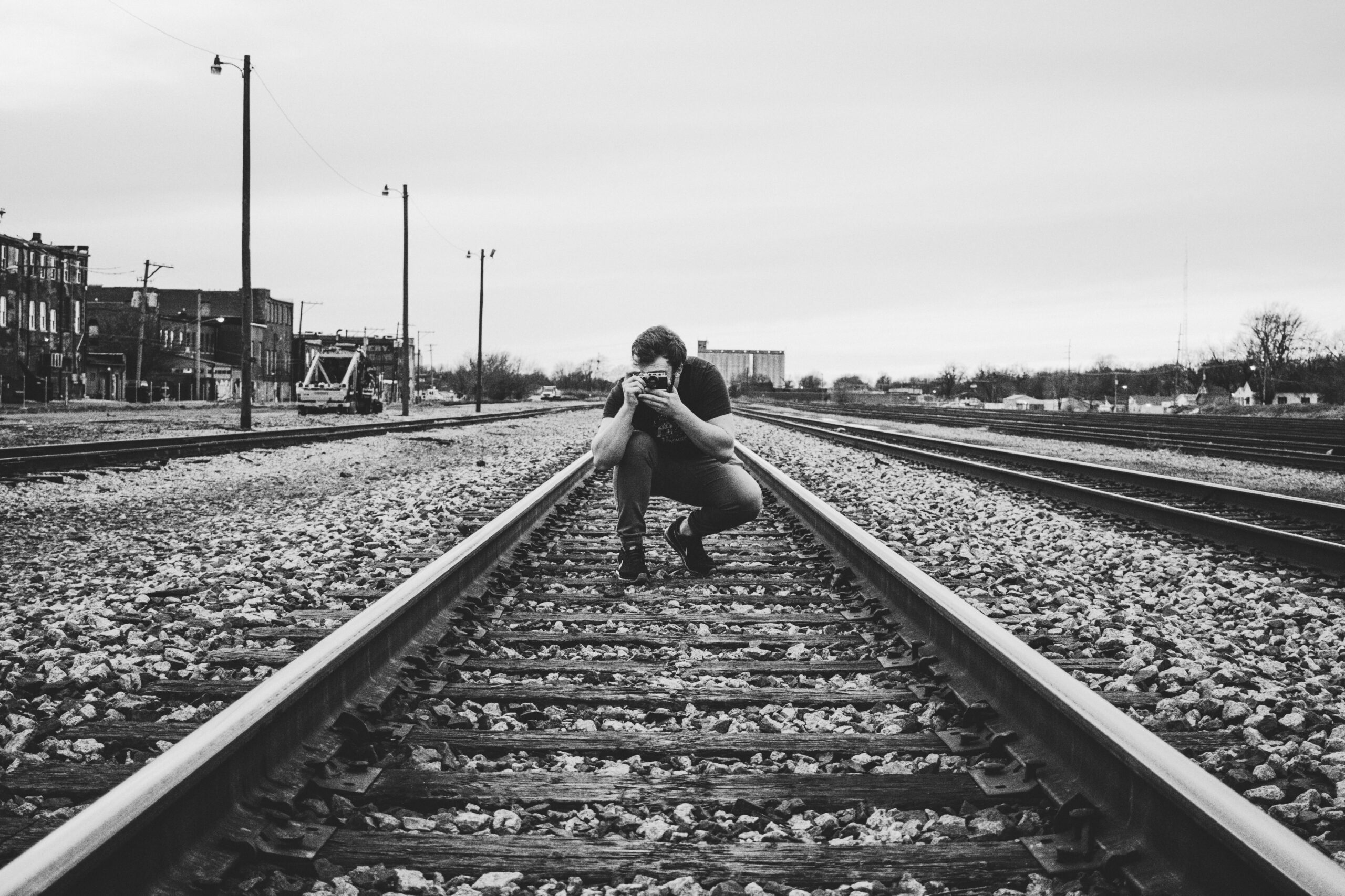A man crouched on train tracks holding a rangefinder camera